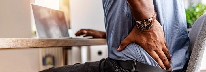 Chiropractic Fremont CA Back Pain A person sitting on a chair, holding their lower back.